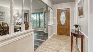 A spacious hallway with a wooden floor, a chandelier, and a wooden door with a glass panel. - “Spacious 4BR Home with Private Pool Perfect for Families!” (San Antonio)