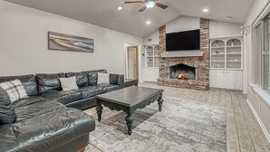 A living room with a fireplace, a black leather sofa, and a ceiling fan. - “Spacious 4BR Home with Private Pool Perfect for Families!” (San Antonio)
