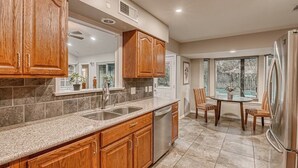 A kitchen with wooden cabinets, a granite countertop, stainless steel appliances, and a dining area with wicker chairs. - “Spacious 4BR Home with Private Pool Perfect for Families!” (San Antonio)