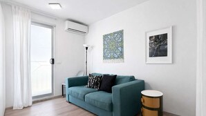 Un salon moderne avec un canapé de couleur turquoise, une petite table d’appoint ronde et un tableau encadré accroché au mur.