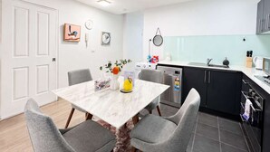 A compact kitchen with a dining area, white walls, and a clock. - Brunswick 1BR: City & Comfort w/ Free Parking (Brunswick)