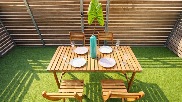 A wooden table with chairs, a potted plant, and a metal ladder against a wooden fence. - Brunswick 1BR: City & Comfort w/ Free Parking (Brunswick)