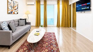 A modern living room with a grey sofa, a patterned rug, a white coffee table, and a large TV screen. - Brunswick 1BR: City & Comfort w/ Free Parking (Brunswick)