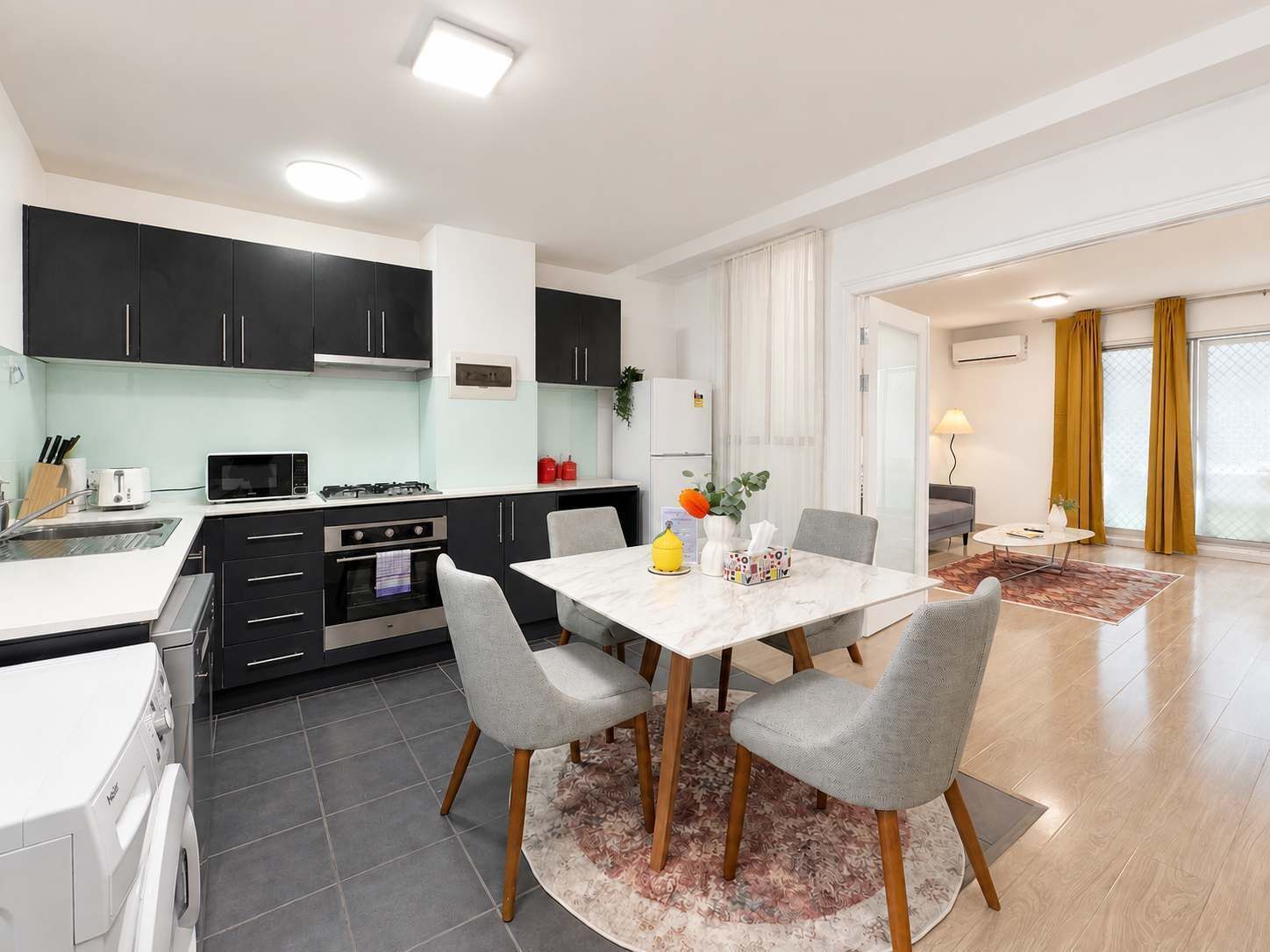 Una cocina moderna con comedor, que incluye una mesa con sillas, una lavadora y un refrigerador.