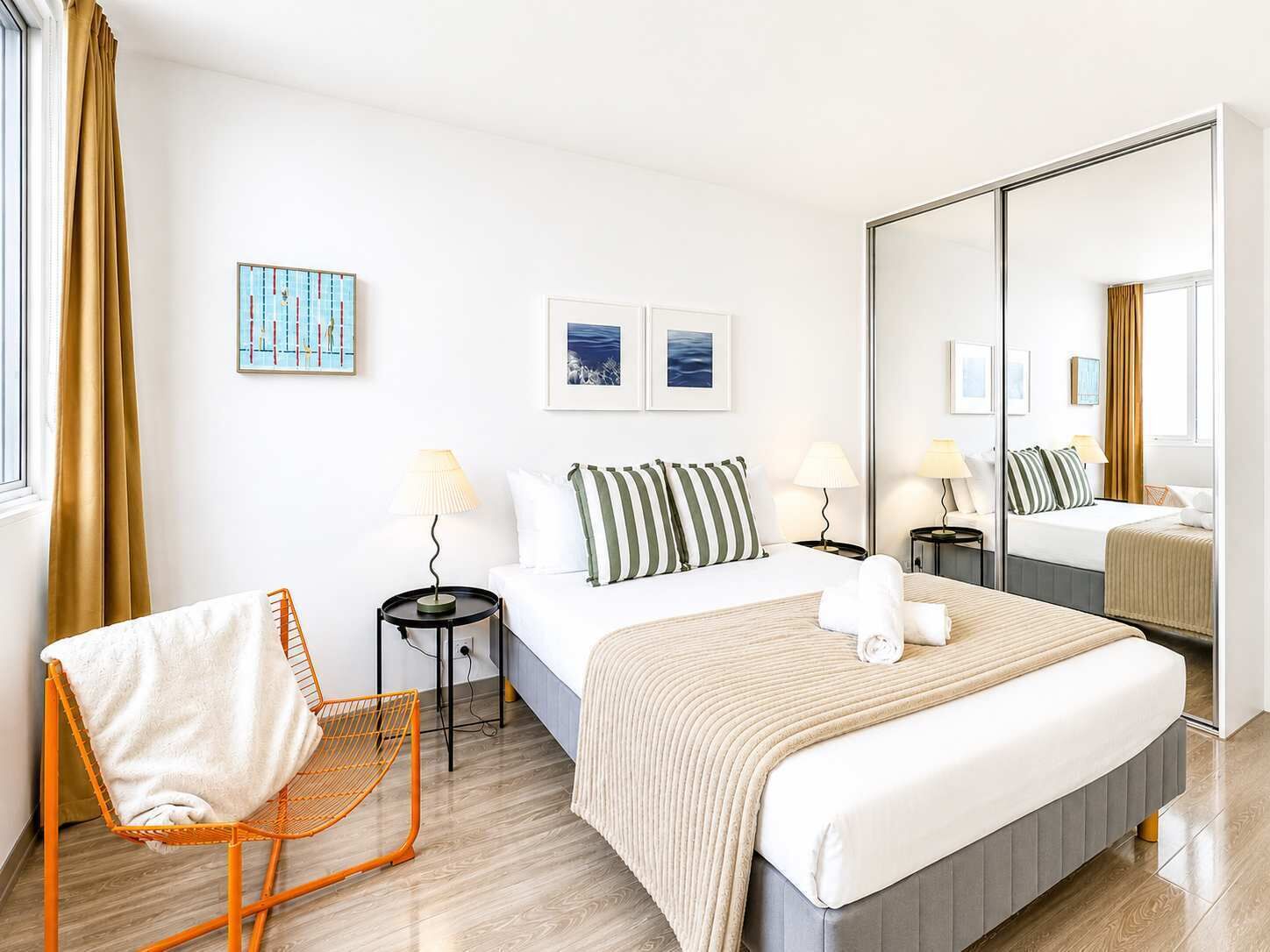 A hotel room with a bed, a chair, a mirror, and artwork on the walls.