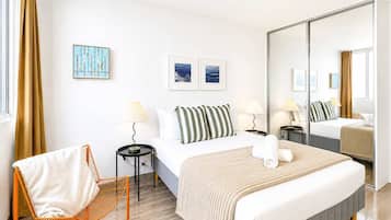 A hotel room with a bed, a chair, a mirror, and artwork on the walls.