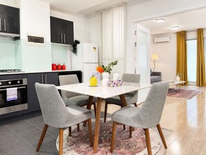 A modern kitchen with a dining area, featuring a white table, grey chairs, and a kitchen island with a refrigerator.