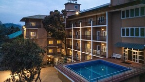 Ett hotell med flera våningar, en swimmingpool, balkonger och utsikt över det omgivande landskapet.