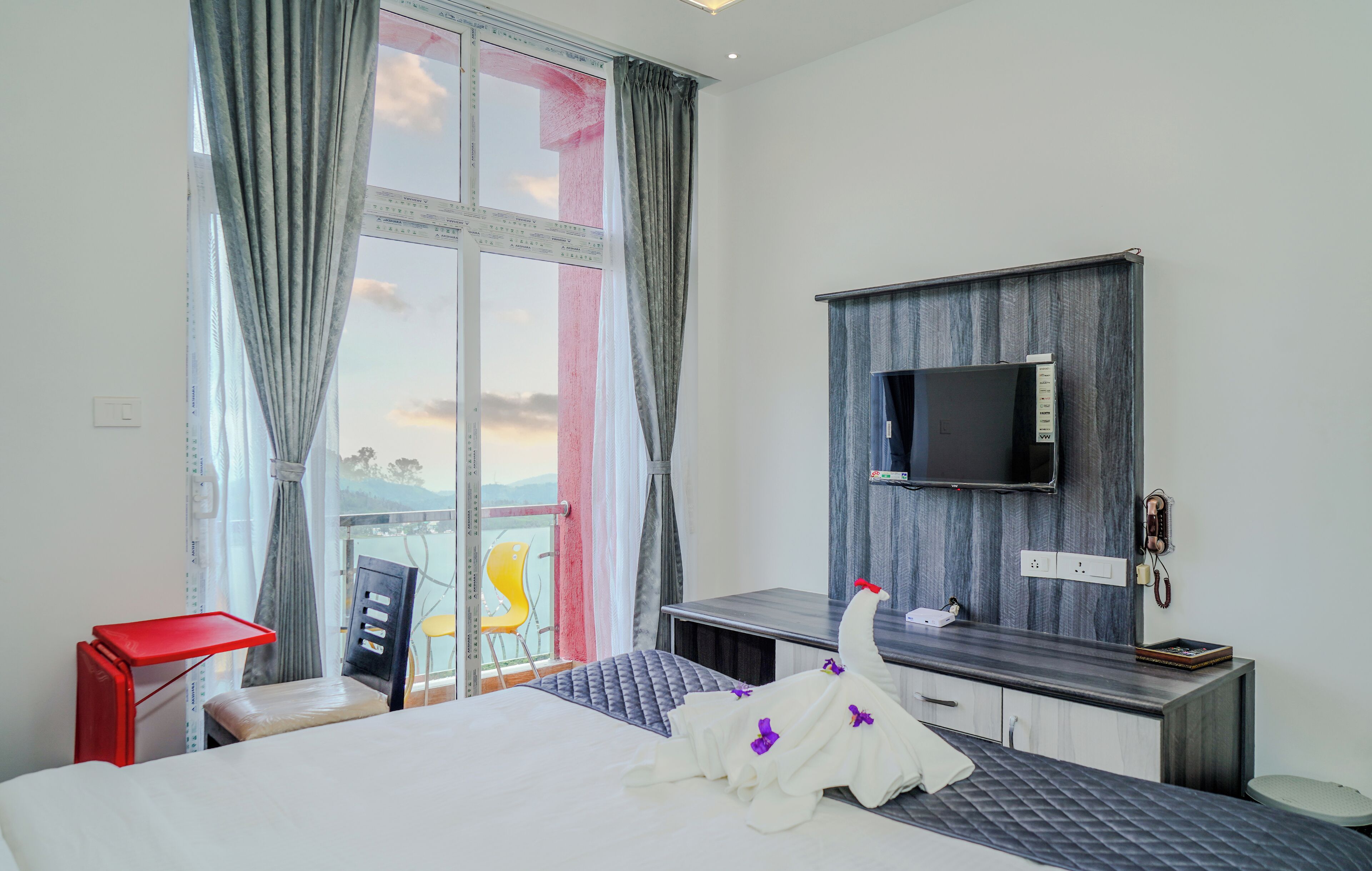 A hotel room with a bed, a desk, a TV mounted on the wall, and a window with curtains.