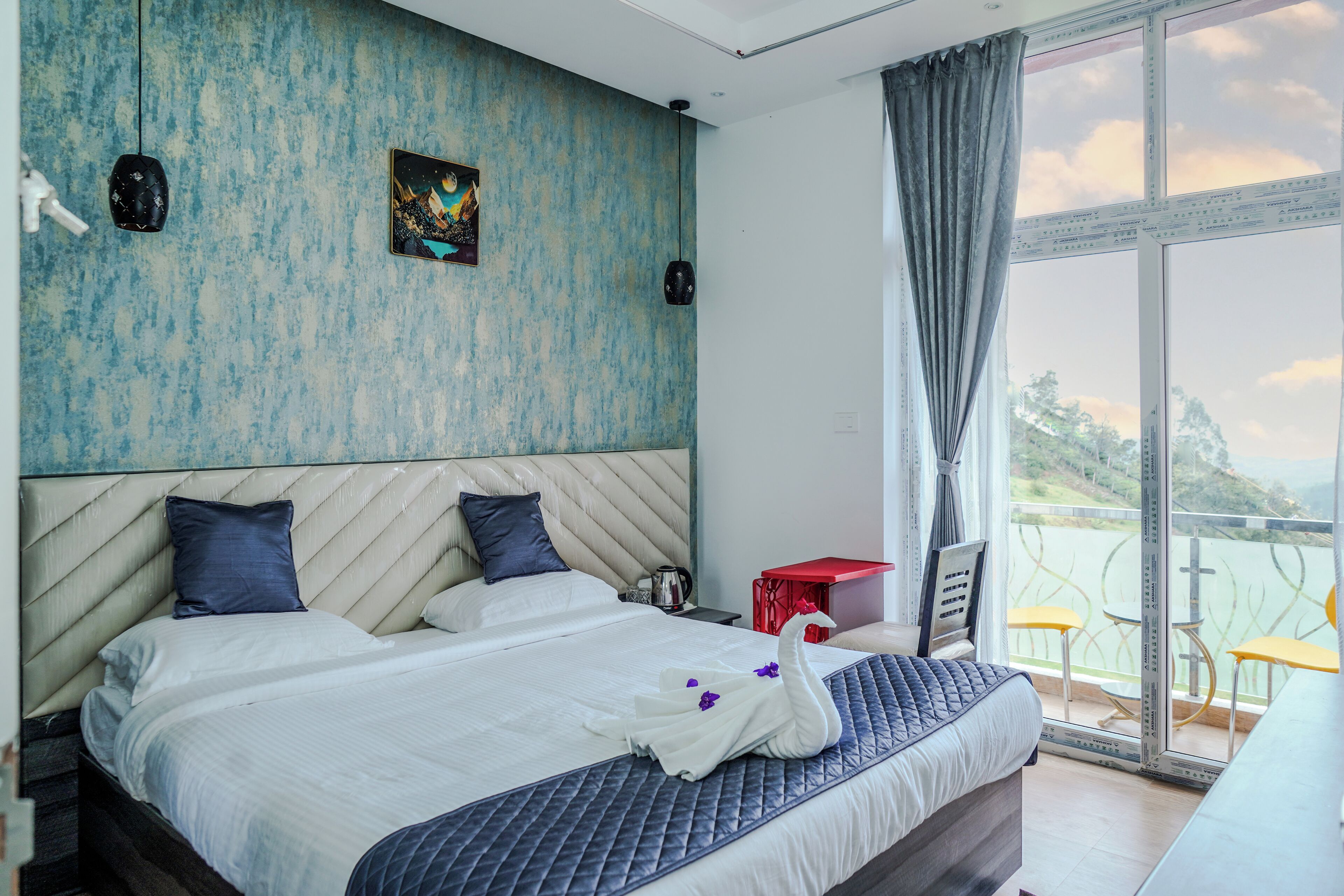 A hotel room with a large bed, a view of the sea, and a red table with yellow chairs.