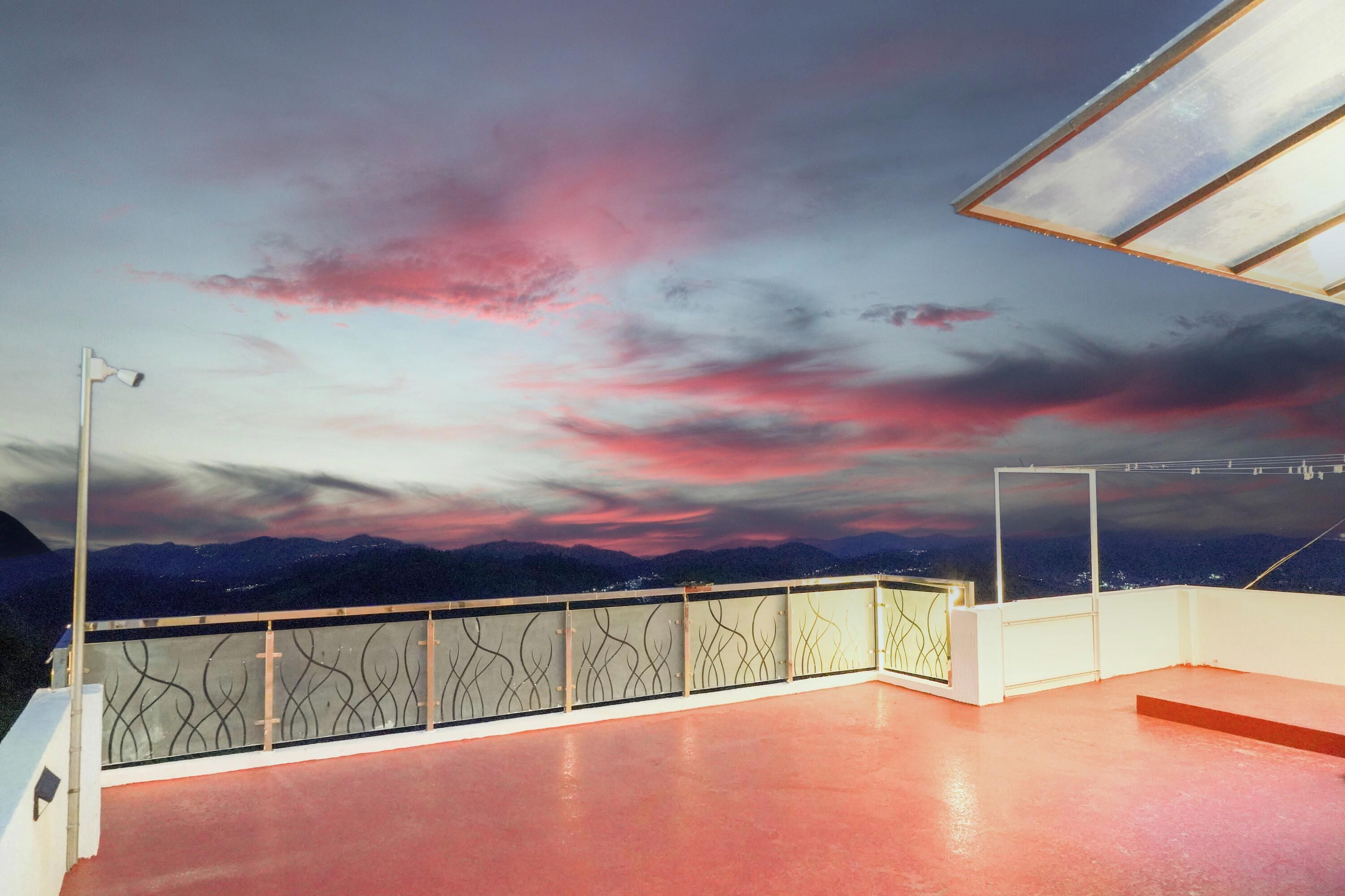 Terraço no telhado com vista para montanhas sob um céu rosa e roxo.