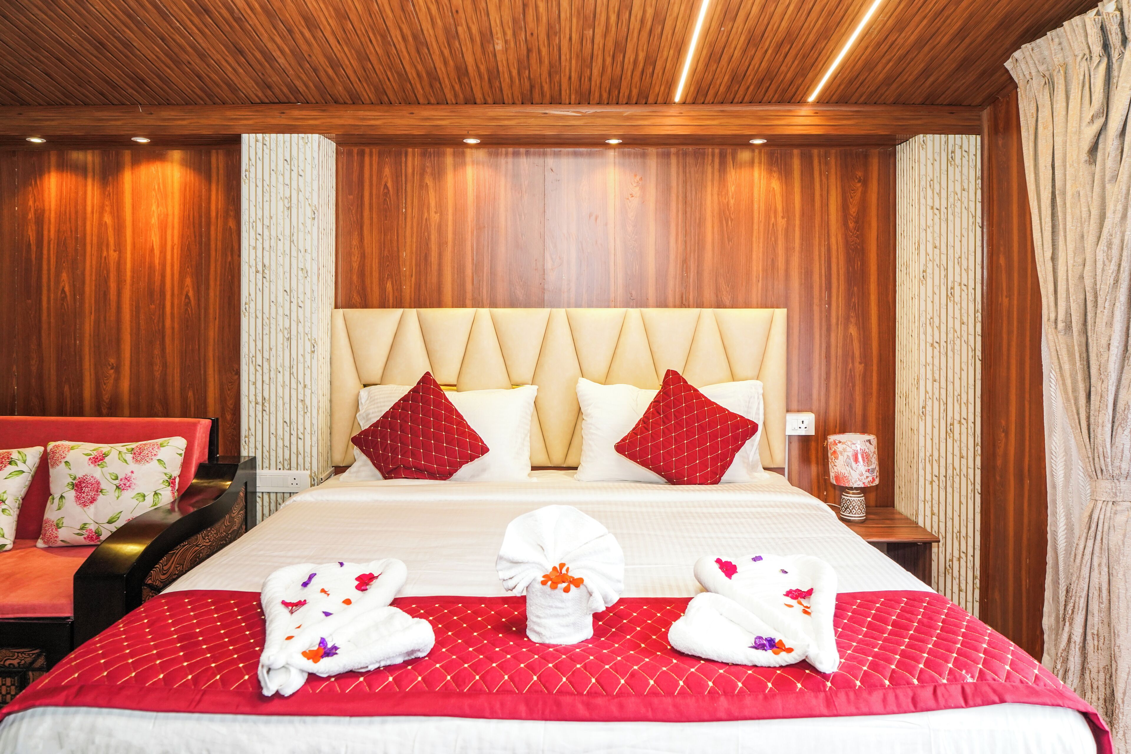 Una camera d'albergo con un letto grande, biancheria rossa e bianca, una testiera in legno e un divano rosso.
