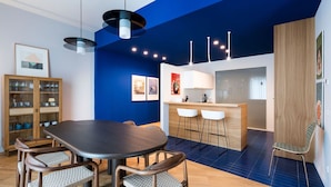 A modern kitchen with a central island, bar stools, and a dining area with a dark table and woven chairs.