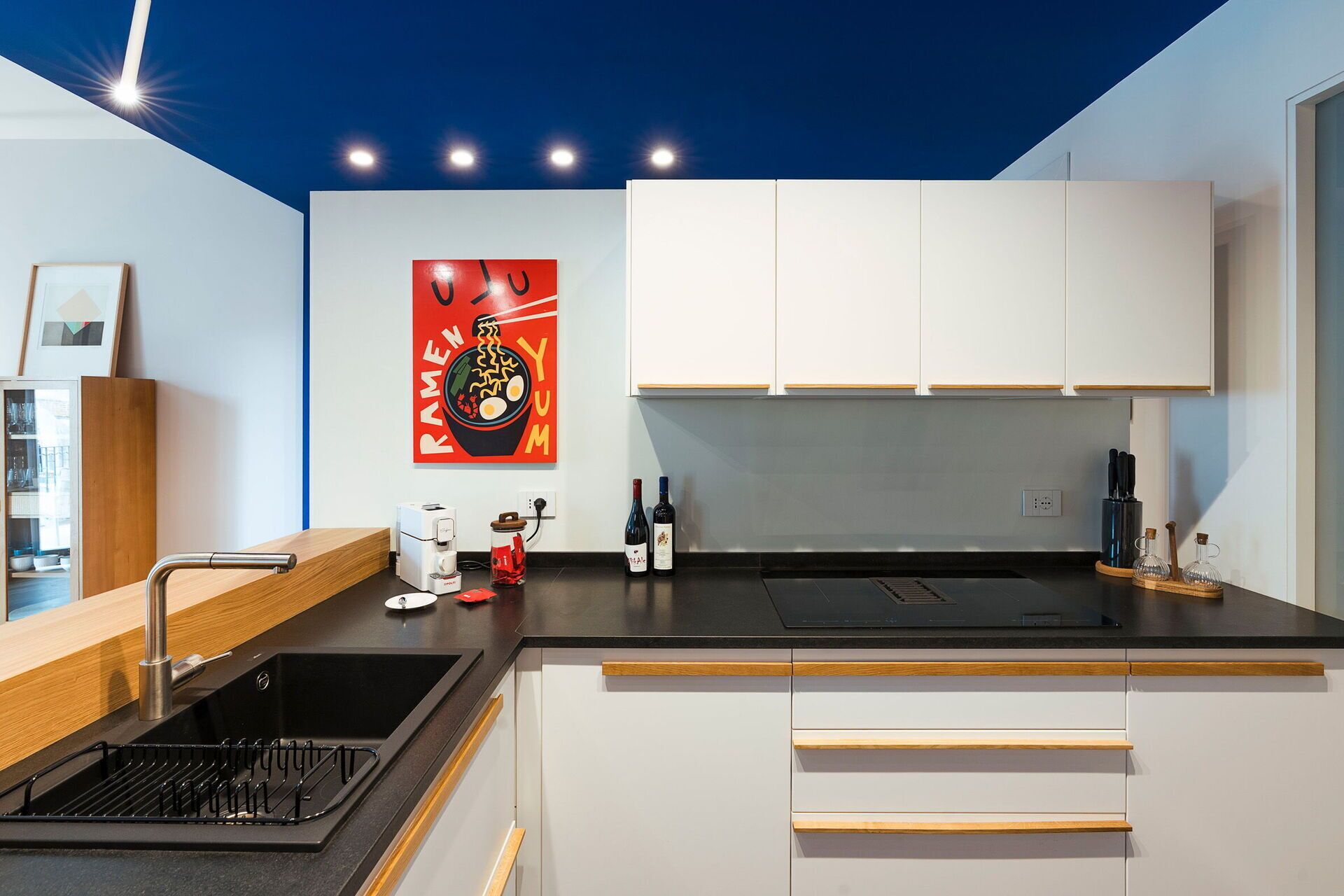 A modern kitchen with white cabinets, a black countertop, and a coffee machine.