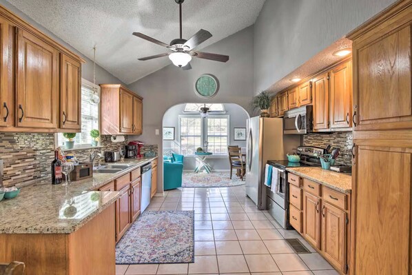 A spacious kitchen with wooden cabinets, granite countertops, and a ceiling fan.