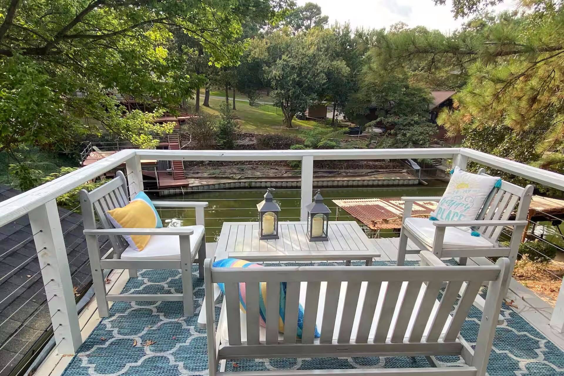 Una terraza con dos sillas de madera blanca y una mesa pequeña, con vistas a un estanque y un jardín.