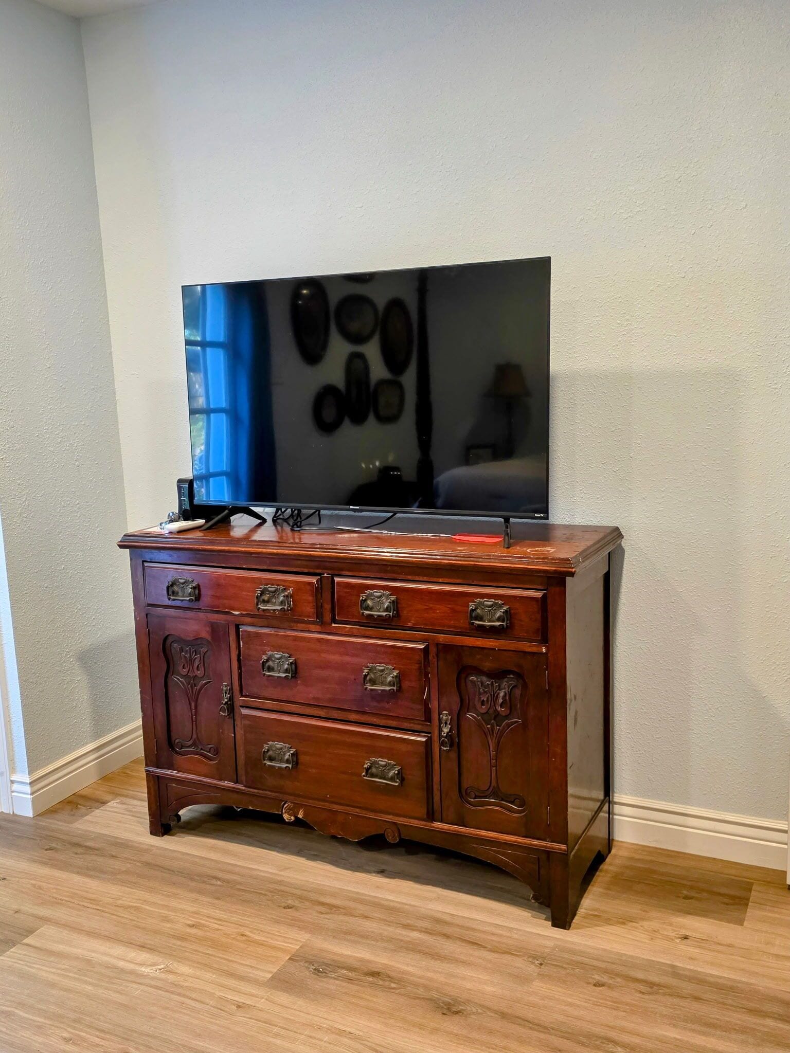 A wooden dresser with multiple drawers and a flat-screen TV mounted on the wall above it.