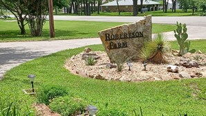 Un cartel que dice 'Robertson Farm' rodeado de un área ajardinada con césped, rocas y cactus.