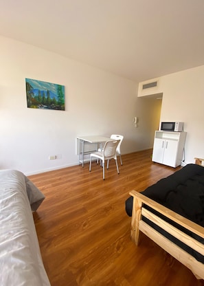 Een kamer met een bed, een bureau, een stoel, een magnetron en een kast.