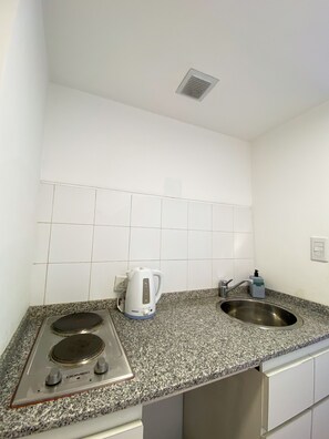 Een keuken met een fornuis, waterkoker, spoelbak en een betegelde spatwand.