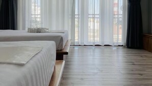 Une chambre d’hôtel avec deux lits, un plancher en bois et de grandes fenêtres ornées de rideaux légers.