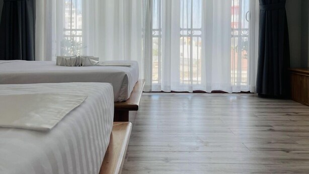 Une chambre d’hôtel avec deux lits, un plancher en bois et de grandes fenêtres ornées de rideaux légers.