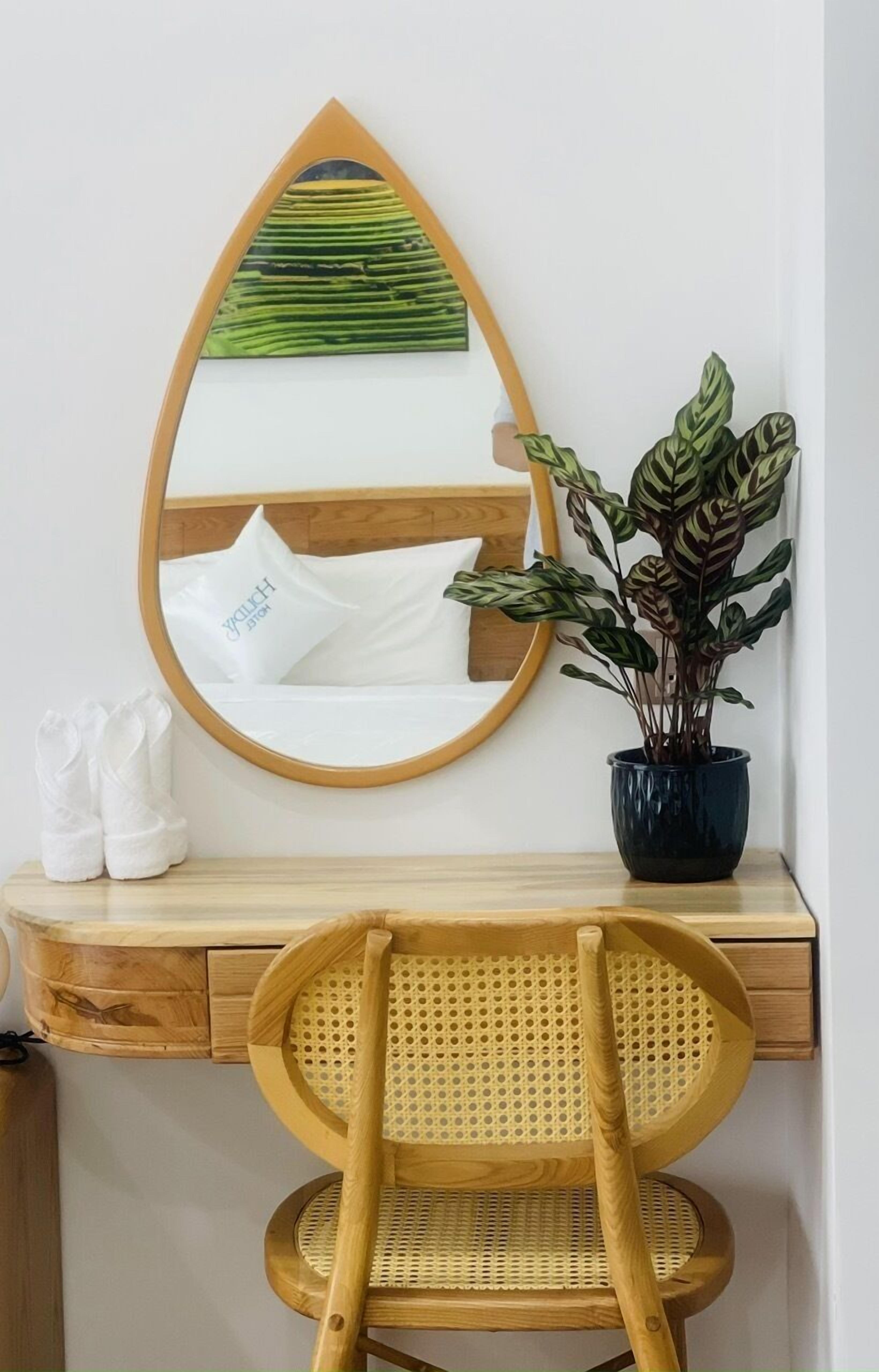 A wooden desk with a mirror, a potted plant, a wicker chair, and a pair of white slippers.