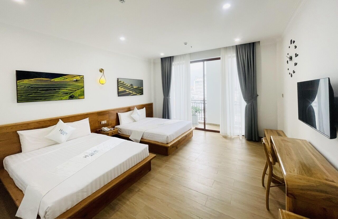Habitación de hotel con dos camas, un escritorio de madera y un ventanal grande con cortinas.