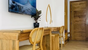 Une pièce moderne avec un bureau en bois, deux fauteuils en osier, un grand tableau encadré, une petite plante en pot et une porte en bois.