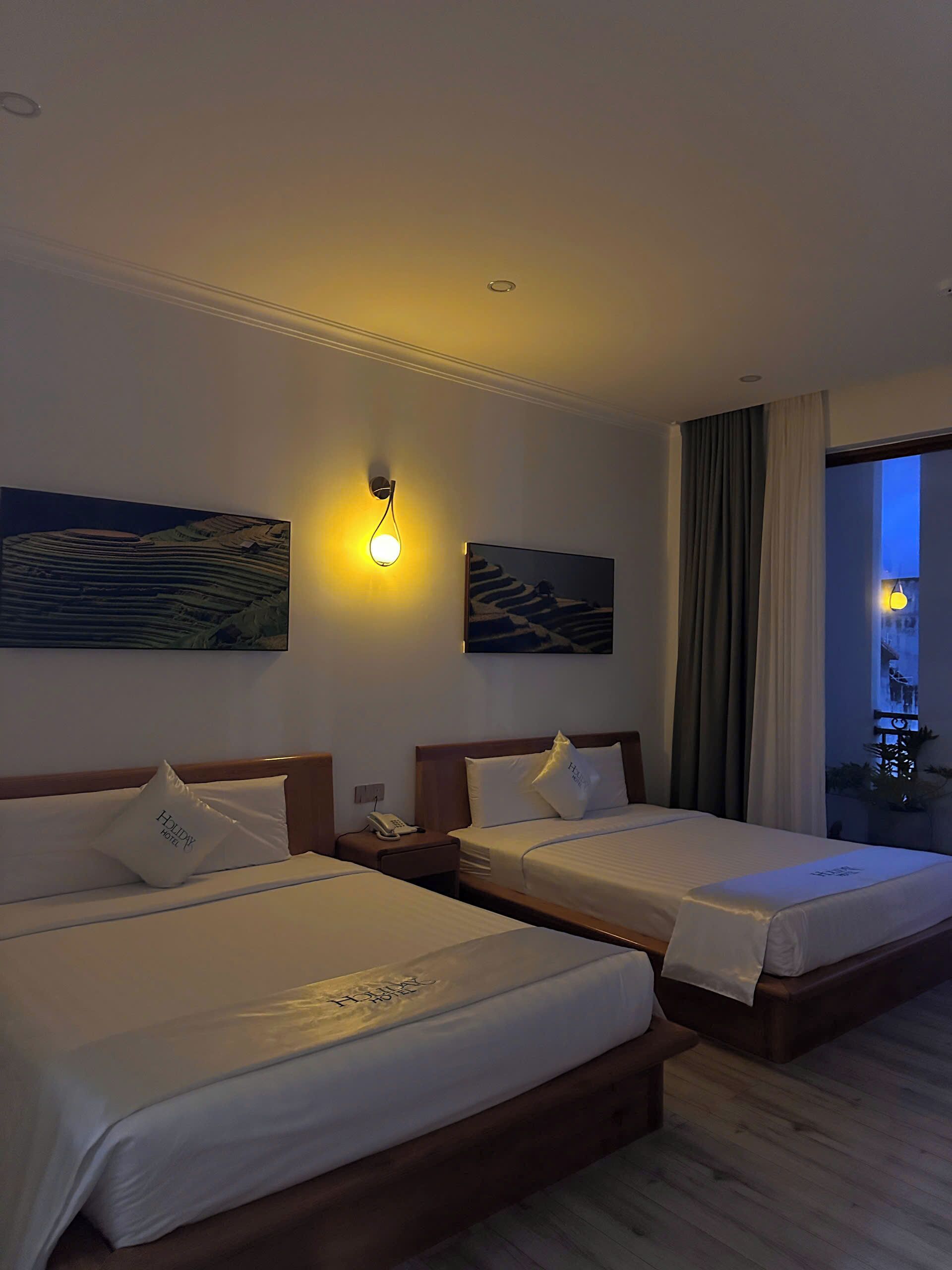 Una habitación de hotel con dos camas, una mesita de noche con un teléfono y obras de arte en las paredes.