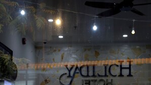 Une cloison en verre portant l’inscription « YALICH HOTEL » et deux chaises en bois avec des assises en osier tressé.