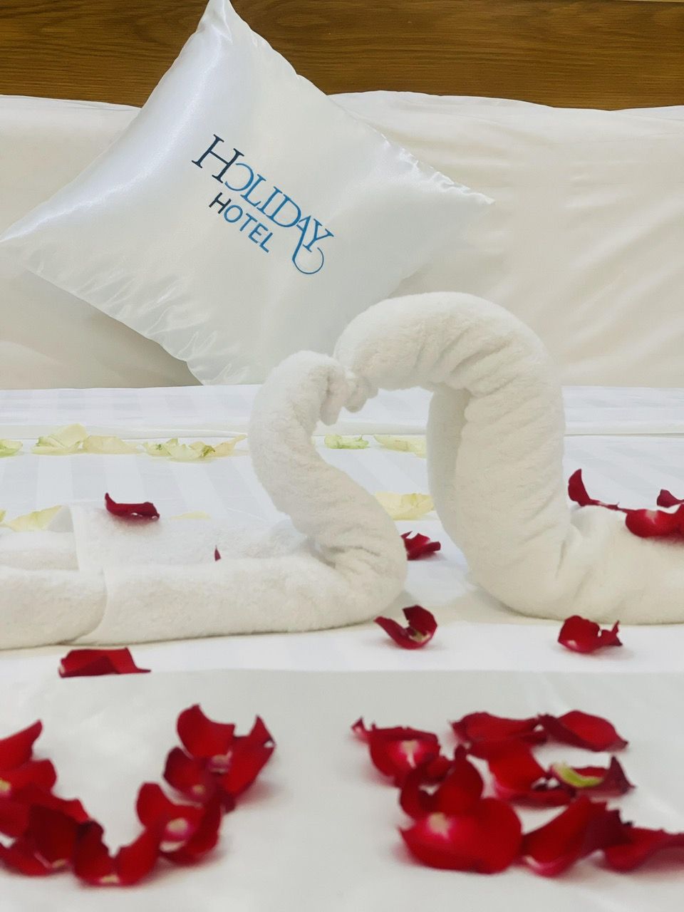 Ein ordentlich bezogenes Bett mit einem Kopfkissen mit der Aufschrift "Holiday Hotel" und zwei schwanenförmigen Handtüchern.