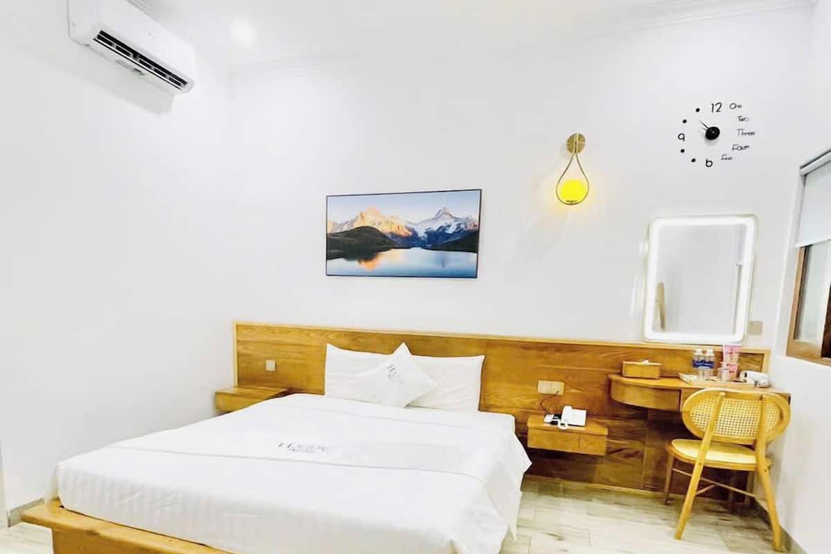 Un dormitorio con cama de madera, un escritorio con silla, un reloj de pared y una fotografía de montañas.
