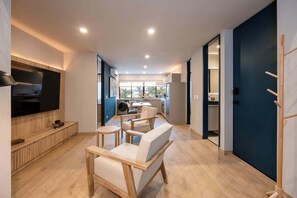 Un apartamento moderno con sala de estar que incluye televisor, muebles de madera y una cocina al fondo.