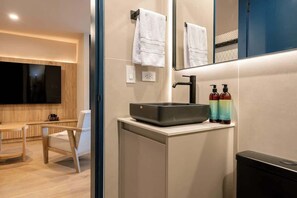 A modern bathroom with a large mirror, a sink with soap dispensers, a towel rack, and a television mounted on the wall.
