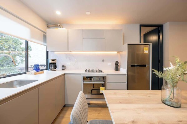 Una cocina moderna con horno empotrado, refrigerador y un comedor con mesa y sillas de madera.