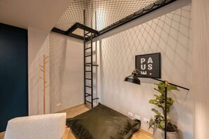 Habitación pequeña con cama en altillo, escalera, una planta y un letrero en la pared.