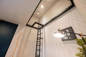 Une pièce avec un mur blanc, une échelle noire, un luminaire noir et un panneau encadré avec du texte.