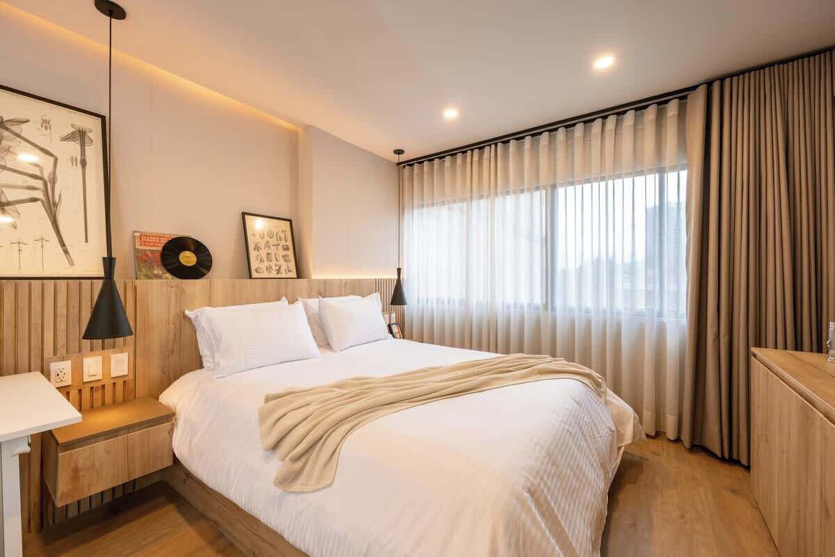 Un dormitorio moderno con una cama grande, mesitas de noche, un escritorio y una ventana con cortinas.