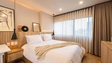 Un dormitorio moderno con una cama grande, mesitas de noche, un escritorio y una ventana con cortinas.