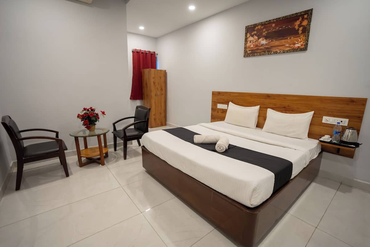 Une chambre d’hôtel avec un grand lit, une petite table ornée de fleurs, une chaise et une armoire en bois.