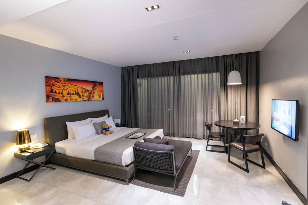 A modern hotel room with a large bed, a desk, a chair, a TV, and a painting on the wall.