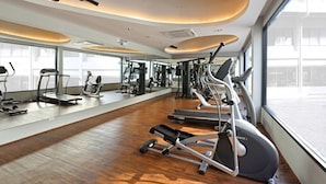 Une salle de sport moderne équipée de machines de cardio, de matériel de musculation et de grandes fenêtres offrant une vue sur la ville.