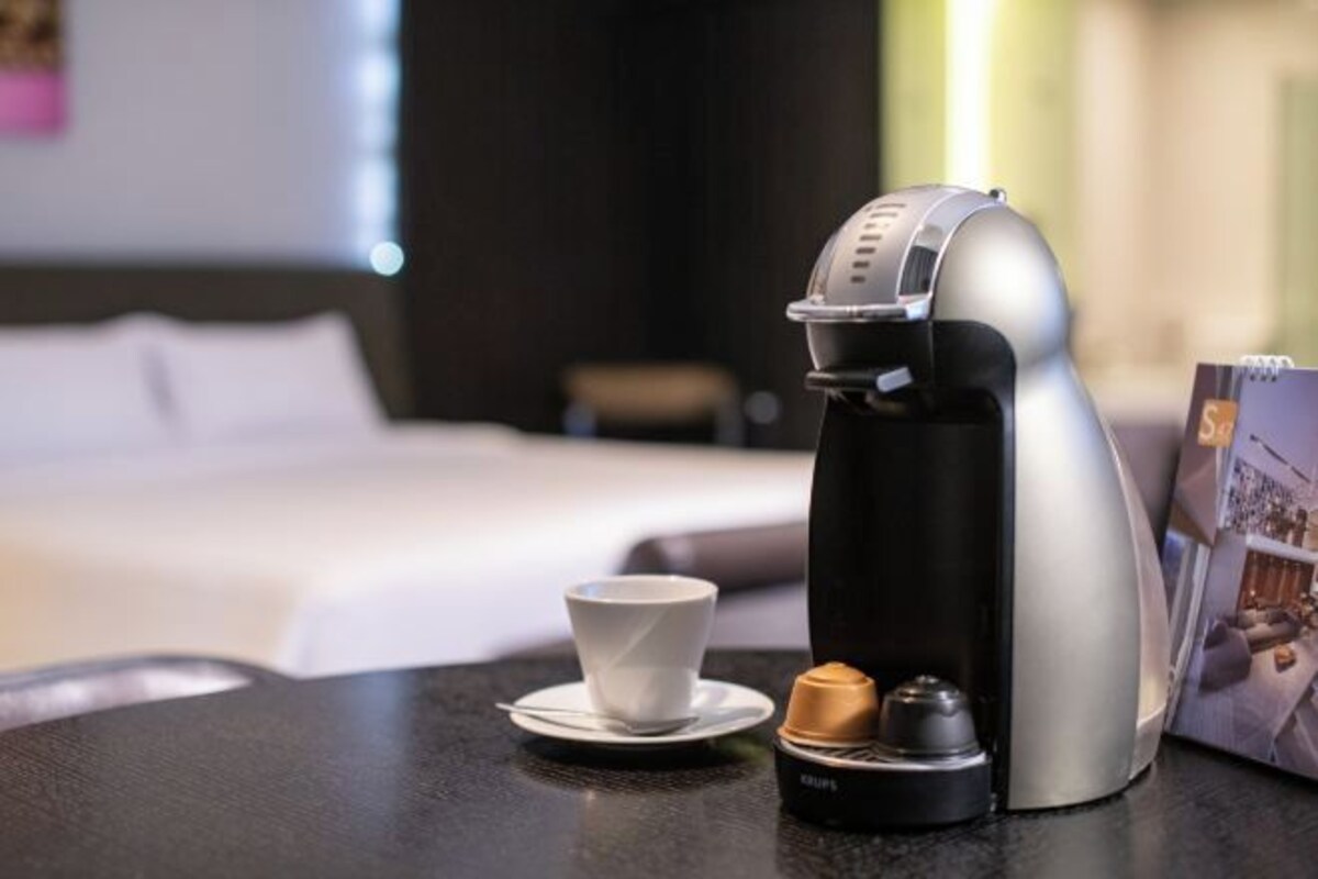 A coffee machine with a cup and saucer, a small container, and a magazine on a table in a hotel room.