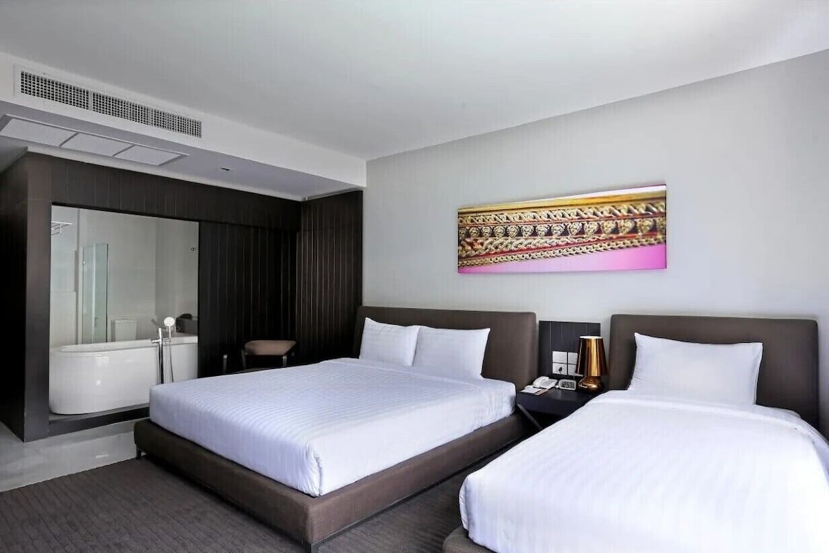 A modern hotel room with two beds, a large mirror, a bathtub, and a decorative wall piece.
