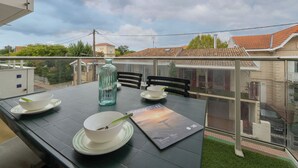 A dining area with a table set for two, a glass bottle, and a menu on a terrace with a view of buildings and trees. - Les Oyats by Interhome (Arcachon)