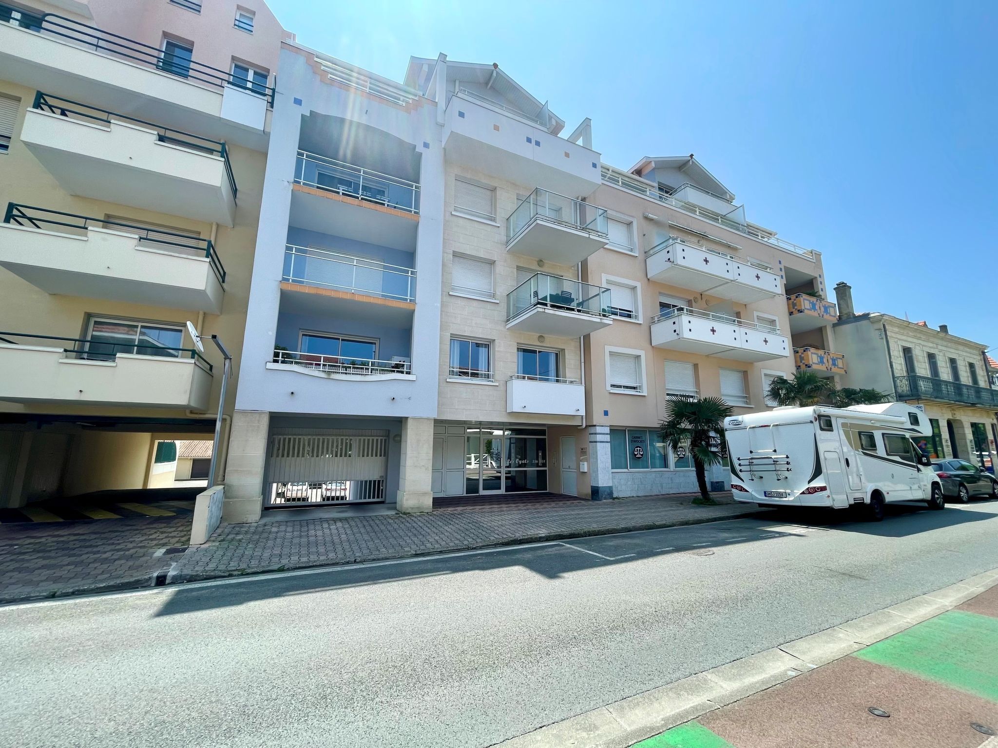 Un edificio residencial de varios pisos con balcones, un acceso con portón y una autocaravana estacionada en la calle.