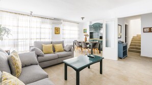A modern living room with a grey sofa, a glass coffee table, and a dining area with a blue cabinet and a staircase. - A&N Marisol (Torre del Mar)
