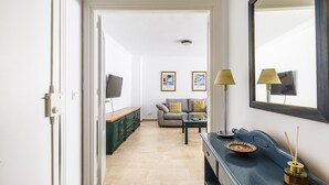 A hallway leading to a living area with a sofa, a coffee table, and a TV. There is a cabinet with drawers and a lamp on the right side. - A&N Marisol (Torre del Mar)