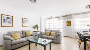 A modern living room with two grey sofas, a glass coffee table, and a dining area with a table and chairs. - A&N Marisol (Torre del Mar)